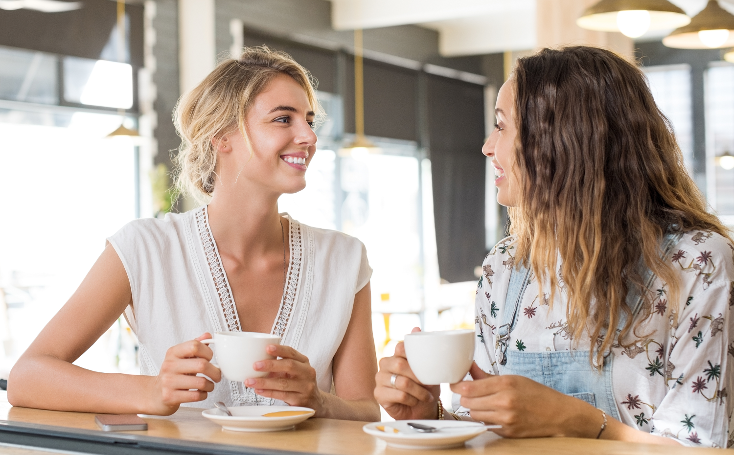 Two women chatting together over coffee in a café as part of an employee wellbeing and staff engagement strategy